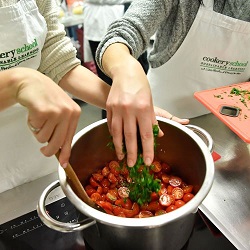 hands sprinkling herbs into pot of tomatoes