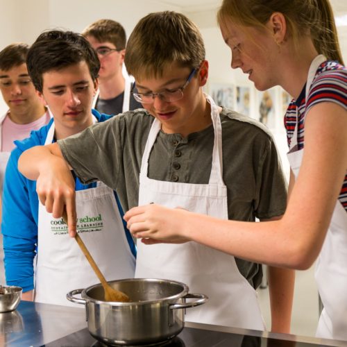 teenagers standing over a hob cooking